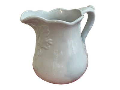 White pitcher with fluted top, high handle, and floral pattern on front.
